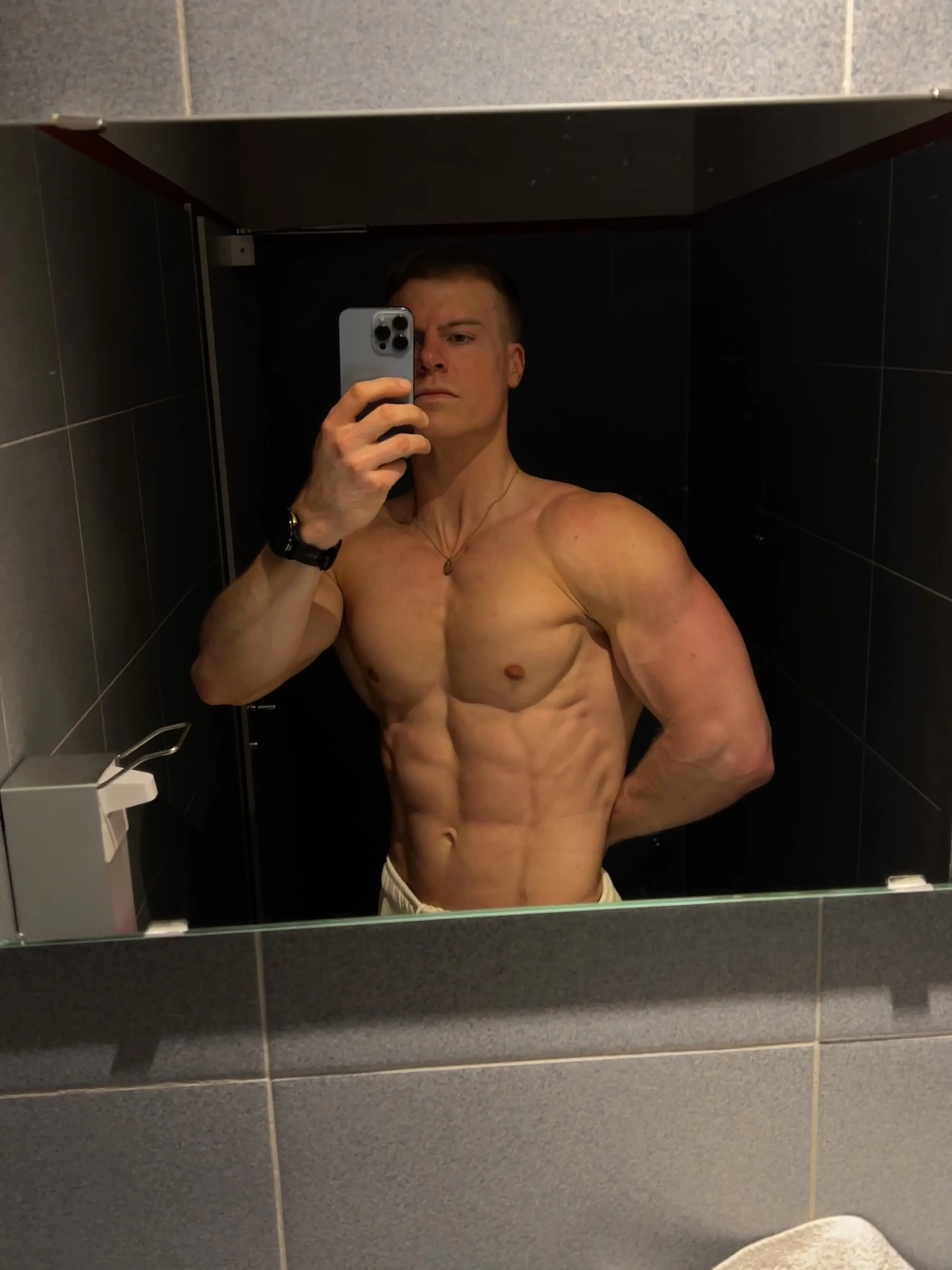 Man taking a mirror selfie in a bathroom, showing his muscular upper body.